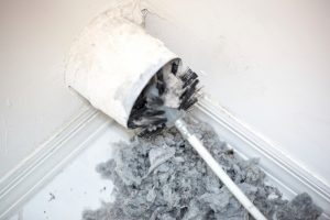Brush cleaning out lint and debris from a home air duct, showing the need for air duct cleaning services.