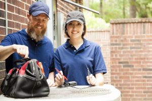 two-technicians-standing-over-outside-ac-unit-with-tool-bag